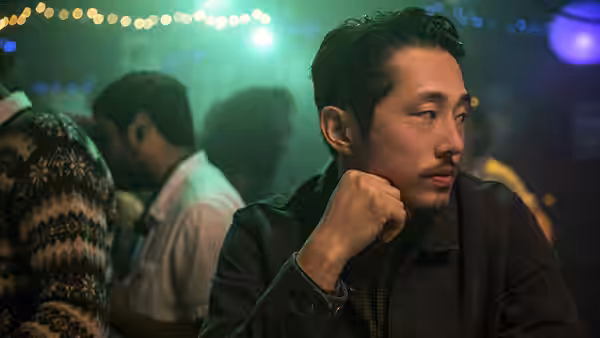 Steven Yeun rests his chin on his fist in a bar