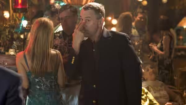 Jack touches his face while speaking with Pam at a crowded party