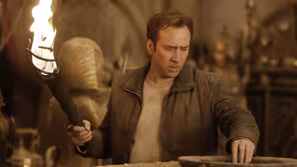 Ben Gates (Nicolas Cage) examines a stone surface by torchlight in a dim underground chamber