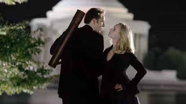 Ben Gates and Abigail Chase stand close together outside a lit white building at night