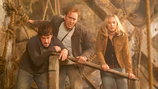 Ben Gates, Riley Poole and Abigail Chase brace against a wooden railing inside a ship