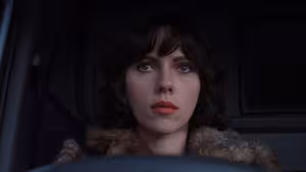 Scarlett Johansson in a fur coat sitting behind the wheel of a car