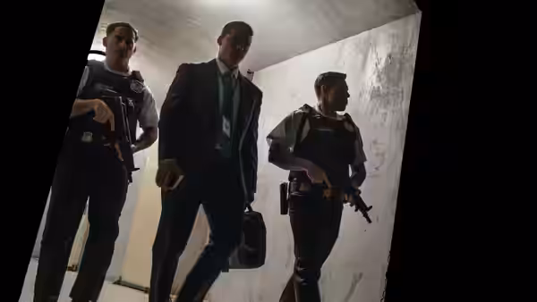 POTUS (Idris Elba) escorted by armed guards through a concrete corridor