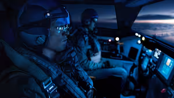 Two pilots in flight suits inside an aircraft cockpit at dusk