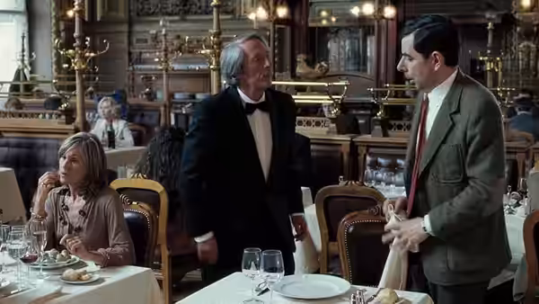 Mr. Bean (Rowan Atkinson) speaks with a maître d'hôtel in an ornate restaurant