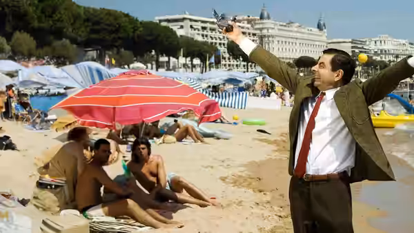 Mr. Bean (Rowan Atkinson) raises his arms on a crowded beach