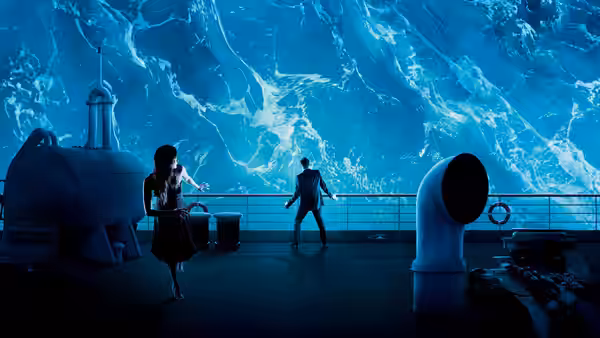 Two passengers stand on deck as a towering wall of water crashes over the railing