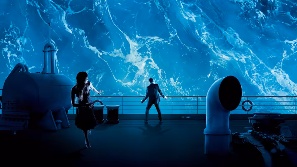 Two passengers stand on deck as a towering wall of water crashes over the railing