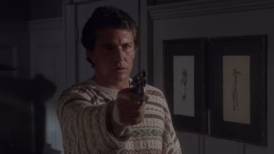 Dan Merrick (Tom Berenger) aims a handgun inside a dimly lit room