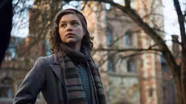 Young Joan (Sophie Cookson) looks across a wooded courtyard toward a large building