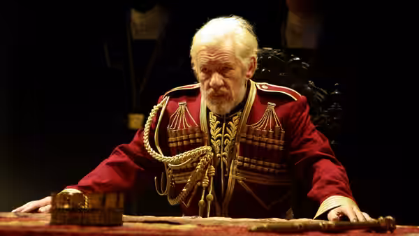 King Lear (Ian McKellen) leans over a table in an ornate red military uniform