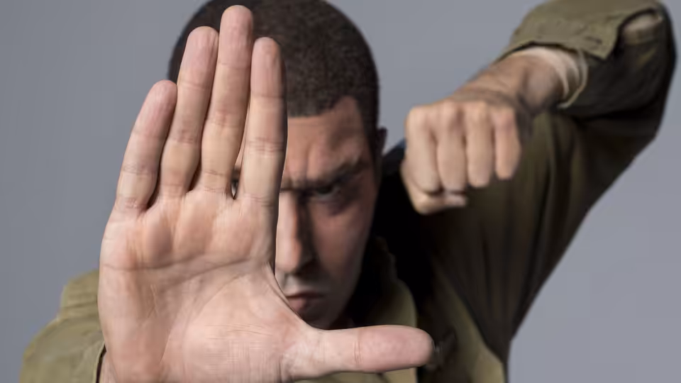 A man in olive clothing raises an open hand and clenches his other fist