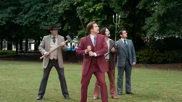 Ron Burgundy and the news team stand armed with tools on a lawn