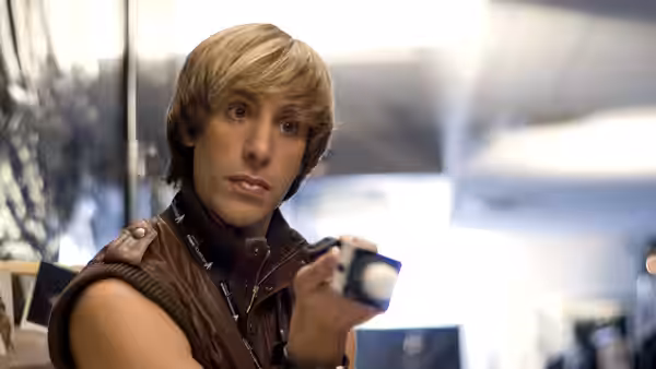 Brüno (Sacha Baron Cohen) holds a small camera in a bright room
