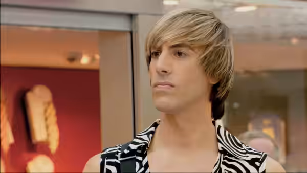 Brüno (Sacha Baron Cohen) stands in a zebra-print shirt by glass doors