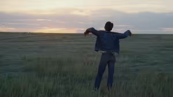 Kit (Martin Sheen) standing with arms outstretched in an open field
