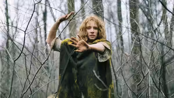 Noah Percy (Adrien Brody) raises his hands among bare trees in the forest