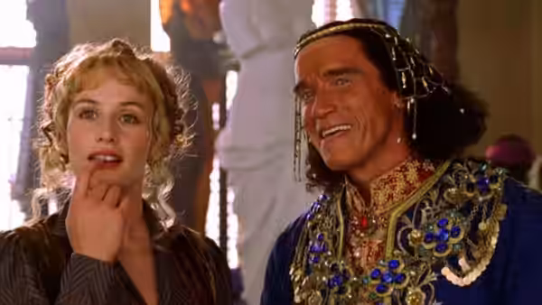 A woman touches her lips beside a smiling man in ornate jeweled clothing