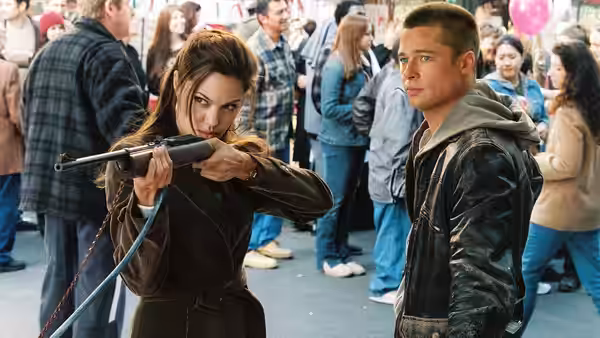 Jane Smith (Angelina Jolie) aims a rifle beside John Smith (Brad Pitt) in a crowded public space