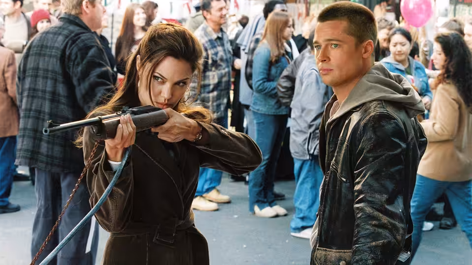 Jane Smith (Angelina Jolie) aims a rifle beside John Smith (Brad Pitt) in a crowded public space