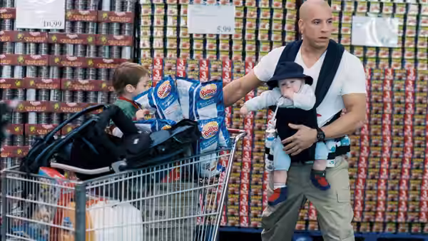 Shane Wolfe (Vin Diesel) holds a baby beside a grocery cart stacked with supplies