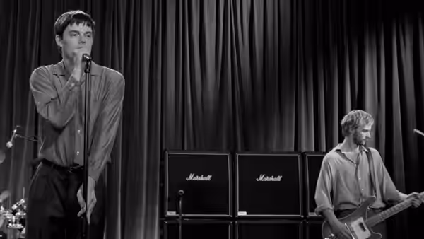 Ian Curtis (Sam Riley) sings into microphone on stage with guitarist