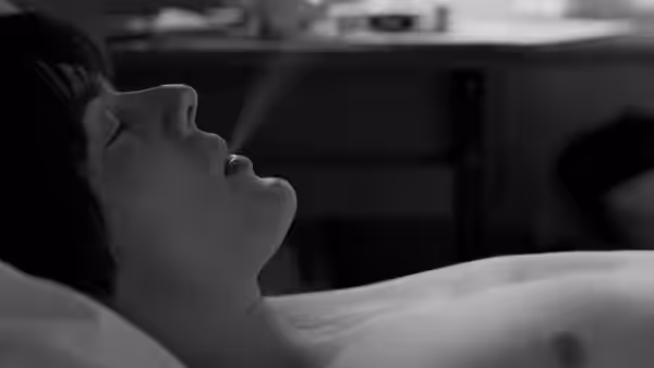 shirtless man lies back with eyes closed exhaling smoke