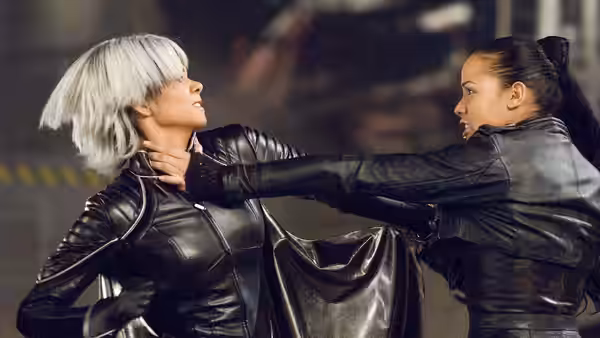 Storm (Halle Berry) grabs a dark-haired woman by the throat in a dim interior