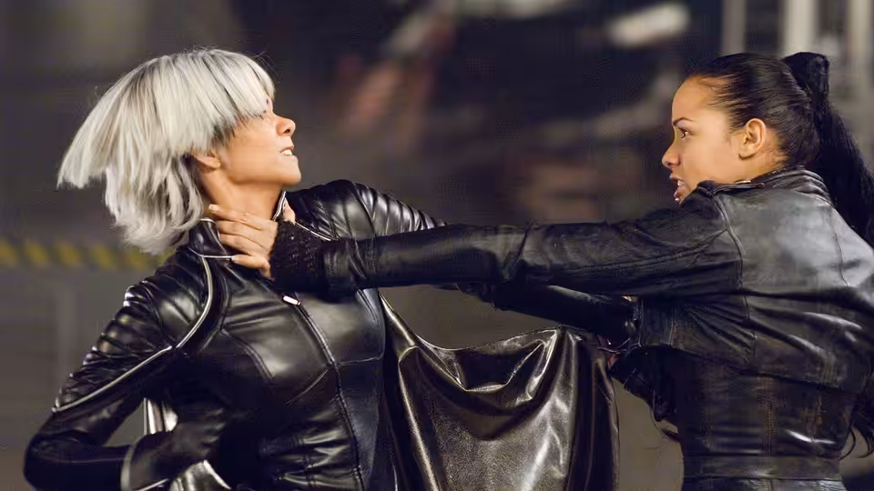 Storm (Halle Berry) grabs a dark-haired woman by the throat in a dim interior