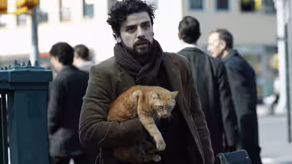 Llewyn Davis (Oscar Isaac) carrying an orange cat along a city sidewalk