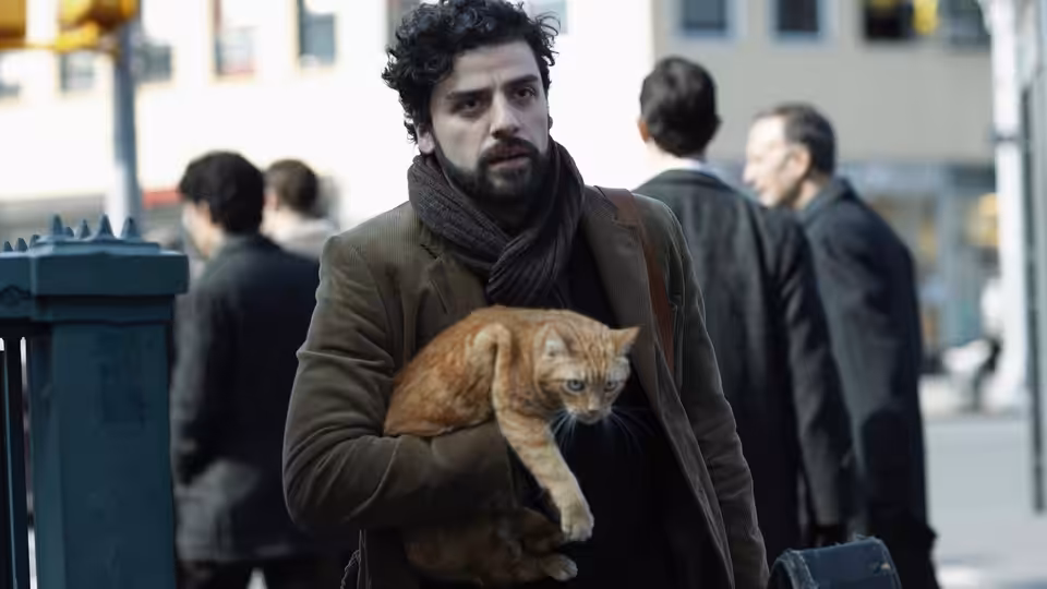 Llewyn Davis (Oscar Isaac) carrying an orange cat along a city sidewalk