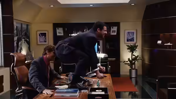 Michael Newman (Adam Sandler) vaults across an office desk as a coworker watches