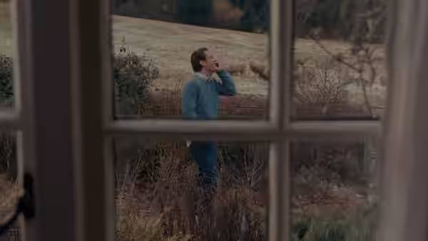 Graham (Jude Law) calls out in the garden, seen through a window