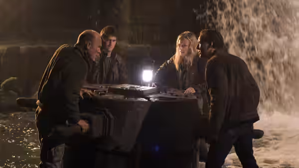 Ben Gates, Riley Poole, Abigail Chase, and another man gather around a table in a flooded chamber