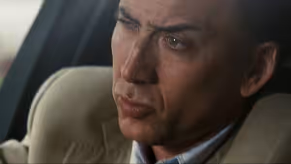 A man in a beige suit sits in a vehicle, looking intently to the side