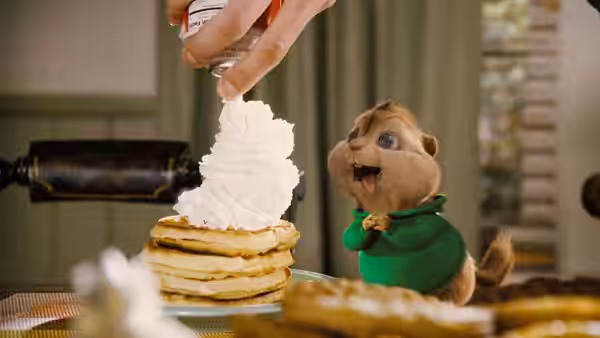 Theodore watches whipped cream pile onto pancakes on a kitchen counter