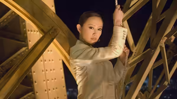 A woman in a light suit climbs a yellow metal framework