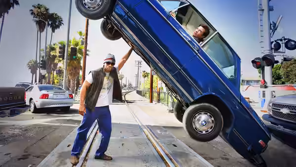John Hancock (Will Smith) holds a blue car tilted above the railroad tracks