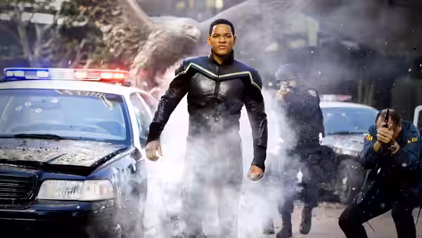 John Hancock (Will Smith) walks through smoke beside a police car as an officer shields himself