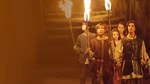 Peter Pevensie leads his siblings and Prince Caspian through a torchlit passage