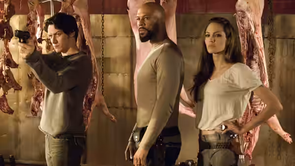 Wesley Gibson, the Gunsmith, and Fox stand among hanging carcasses as Wesley aims his gun