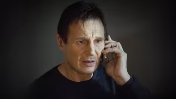 Bryan Mills (Liam Neeson) speaks on a phone against a dark wall