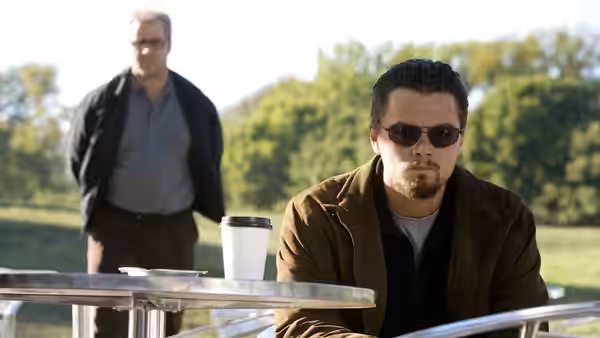 Roger Ferris (Leonardo DiCaprio) sits at an outdoor table as Ed Hoffman (Russell Crowe) stands behind him