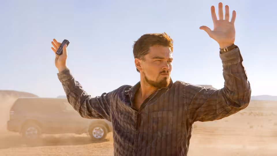 Roger Ferris (Leonardo DiCaprio) raises his hands in the desert, holding a phone in one hand