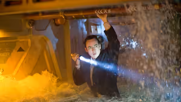 Jackson Curtis (John Cusack) clings beneath heavy machinery amid rushing water