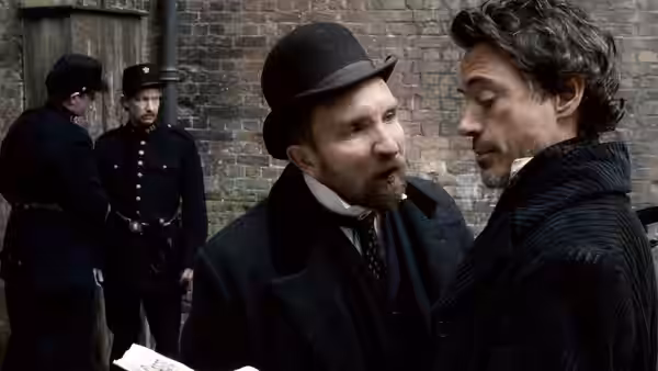Inspector Lestrade (Eddie Marsan) speaks with Sherlock Holmes (Robert Downey Jr.) beside uniformed constables