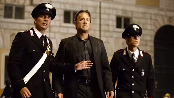 Robert Langdon (Tom Hanks) walks between two uniformed guards outside a stone building