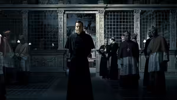 A priest stands before a group of clergy inside an ornate chapel