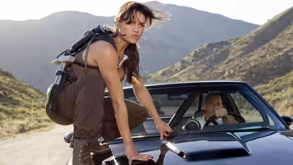 Letty Ortiz crouches on a car hood while Dominic Toretto drives through the mountains