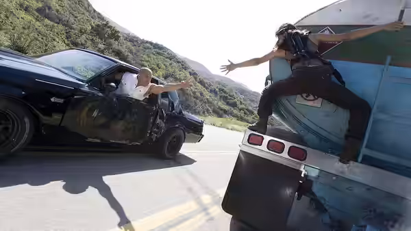 Dominic Toretto reaches from his car toward Letty Ortiz perched on a truck